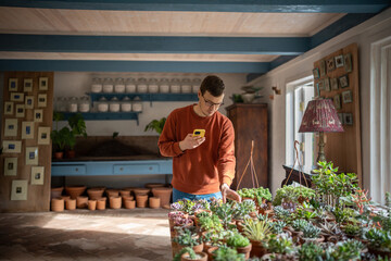 Young man buying succulent at mother, wife request, making photo with smartphone, sending snapshot...
