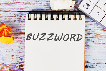 Buzzword - word written on a sheet of notebook lying on old vintage boards with a calculator and folded paper