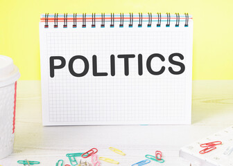 POLITICS the word is written on a blank sheet in a notebook standing on a table on a yellow background