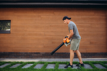 man uses a blower, a vacuum cleaner works in an autumn garden, blowing off fallen leaves from a...