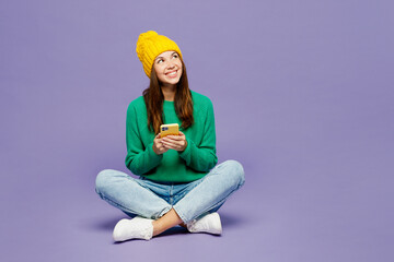 Full body happy young woman wear green sweater yellow hat casual clothes sit hold in hand use...