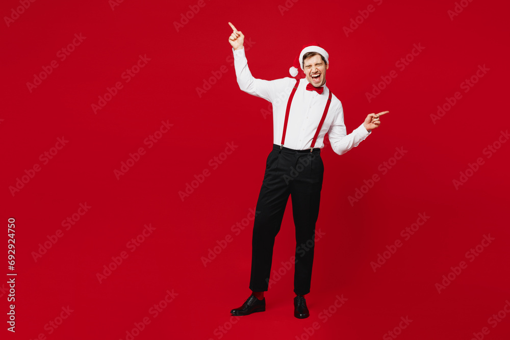 Wall mural full body merry cheerful young man wears white shirt santa hat posing raise up fingers dancing have 