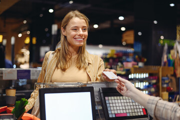 Young customer woman in casual clothes give seller credit bank card at checkout shopping at supermaket store grocery shop buy with trolley cart choose products in hypermarket Purchasing food concept - obrazy, fototapety, plakaty