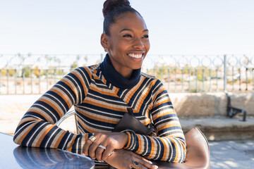 Content young black woman smiling and looking away on cafe terrace