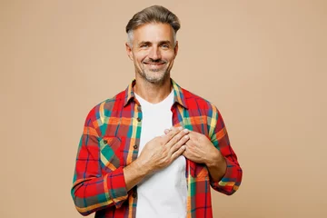  Adult smiling cheerful man wear red shirt white t-shirt casual clothes put folded hands on heart look camera isolated on plain pastel light beige color background studio portrait. Lifestyle concept. © ViDi Studio
