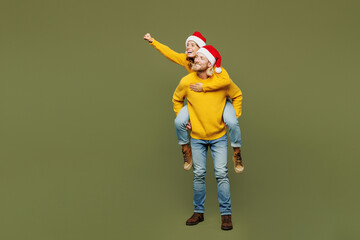 Full body merry young couple two friends man woman wears sweater Santa hat posing giving piggyback...