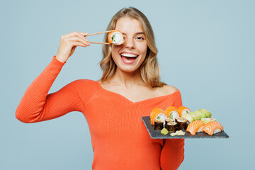 Young happy woman wear orange casual clothes hold cover eye with bar of eat raw fresh sushi roll...