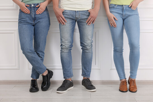 People in stylish jeans near white wall indoors, closeup