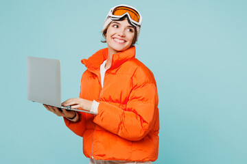 Skier young happy IT woman wear padded windbreaker jacket hat ski goggles mask work hold use laptop pc computer travel rest spend weekend winter season in mountains isolated on plain blue background. © ViDi Studio