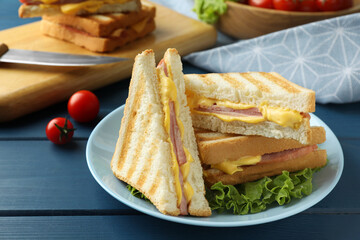 Tasty sandwiches with ham, melted cheese and lettuce on blue wooden table