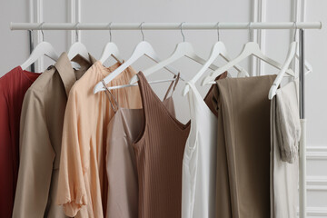 Rack with different stylish women`s clothes near white wall indoors, closeup