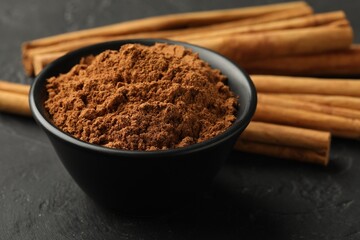 Aromatic cinnamon powder and sticks on black table, closeup