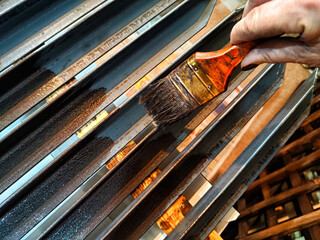 A brush in a woman's hand paints iron metal bars with brown paint. Work and worker