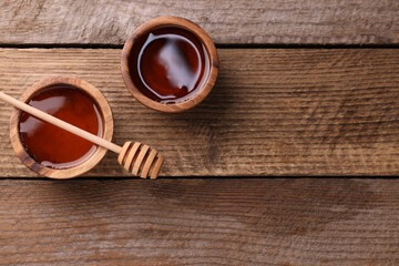 Delicious honey in bowls and dipper on wooden table, flat lay. Space for text