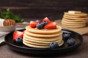 Delicious pancakes with strawberries and blueberries on brown textured table, closeup