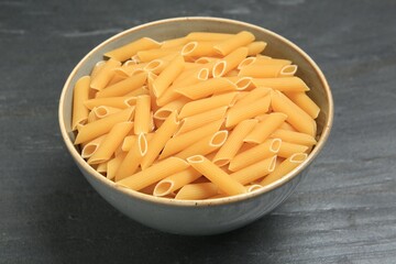 Raw penne pasta in bowl on grey table, closeup