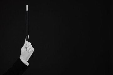 Magician holding wand on black background, closeup. Space for text