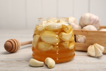 Honey with garlic in glass jar and dipper on light wooden table, closeup