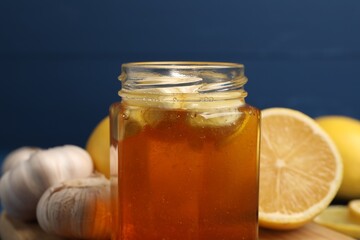 Honey with garlic in glass jar and lemons on table, closeup