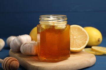 Honey with garlic in glass jar, lemons and dipper on blue wooden table, closeup
