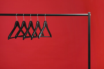Black clothes hangers on rack against red background. Space for text