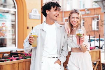 Young smiling beautiful woman and her handsome boyfriend in casual summer clothes. Happy cheerful family. Female having fun. Couple posing in street. Holding and drinking cocktail drink in plastic cup