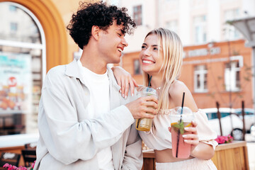 Young smiling beautiful woman and her handsome boyfriend in casual summer clothes. Happy cheerful family. Female having fun. Couple posing in street. Holding and drinking cocktail drink in plastic cup