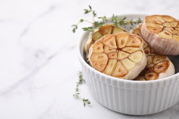 Heads of fried garlic and thyme in bowl on white table, closeup. Space for text