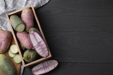 Purple and green daikon radishes in crate on black wooden table, flat lay. Space for text