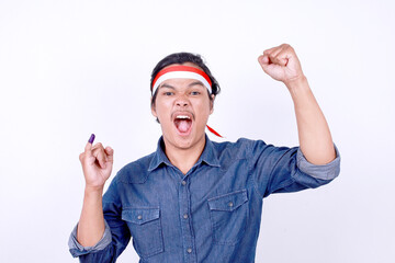 Young man wear headband, raising fist and screaming to the camera while showing little finger after voting in Indonesia election day 