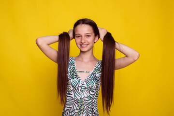 proper long hair care in summer, teen girl make ponytails on yellow studio background. no split ends hair