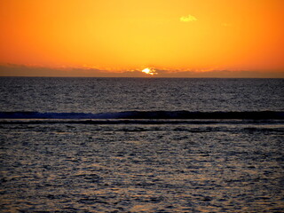Beautiful sunset over Indian ocean, with orange sky and sun disappearing in the clouds, Reunion