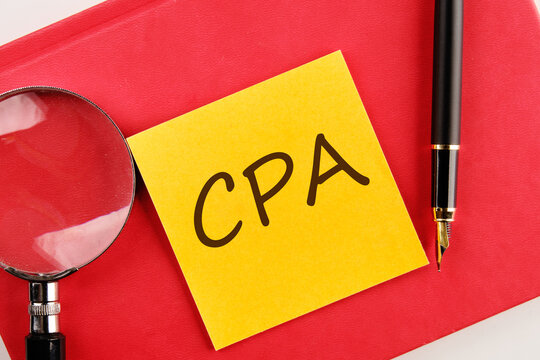 CPA, Certified Public Accountant or Cost per Action the inscription on the sticker lying on a red notebook next to a magnifying glass and a fountain pen