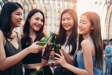 Group of happy Asian girl friends celebrating party with beer bottle toasting drinks at rooftop bar...
