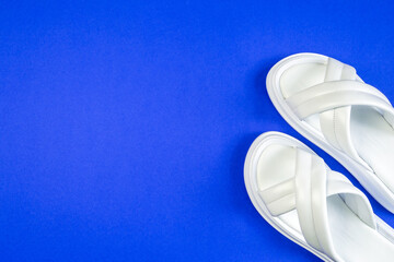 White leather women's slippers stand on a blue background. Slippers are located at an angle. View from above. A part of the shoe is visible. Horizontal image