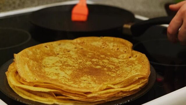 Frying crepes. Making homemade pancakes for family breakfast. Stacking crepe on a plate from a hot pan. Home cooking. Maslenitsa holiday.