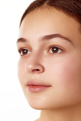 Obraz premium Close-up portrait of beautiful young girl with smooth, healthy, well-kept skin, brown eyes standing against white background. Concept of natural female beauty, skin care, cosmetology and cosmetics