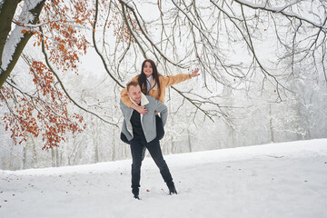 Holding woman that rides him. Beautiful couple are standing together on the snowy field of forest