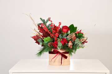 Sombrerera de flores navideña rojas sobre mesa blanca y fondo neutro
