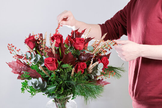 Florista adornando ramo de flores navideño de color rojo sobre fondo neutro 