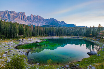 Emerald waters, misty Spruce forests, and breathtaking views define Lago di Carezza, an alpine favourite in Val d'Ega, South Tyrol, and the Dolomites. - obrazy, fototapety, plakaty