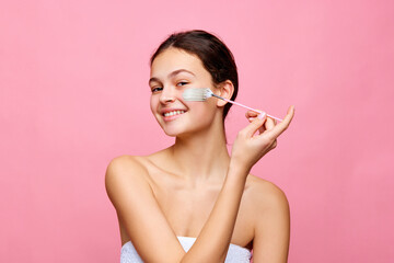 Pretty young girl taking care after skin, applying refreshing and nourishing face mask against pink background. Concept of natural female beauty, skin care, cosmetology and cosmetics
