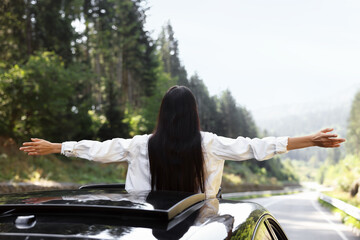 Enjoying trip. Woman leaning out of car roof outdoors, back view
