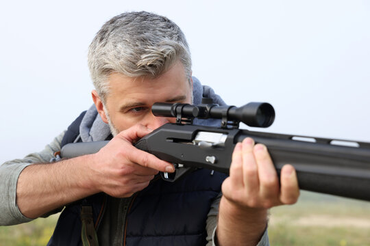 Man aiming with hunting rifle outdoors, closeup