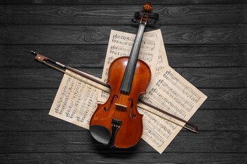 Violin, bow and music sheets on black wooden table, top view