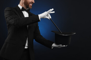 Magician showing magic trick with top hat on dark blue background, closeup