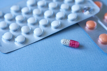 Tablets and capsules in blister pack on blue background. Focus on foreground, soft bokeh.