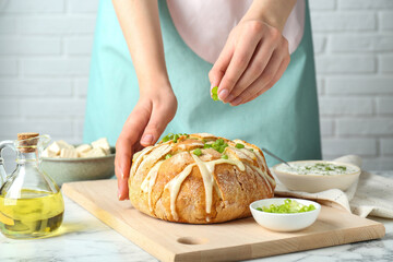 Woman adding green onion onto freshly baked bread with tofu cheese at white marble table, closeup