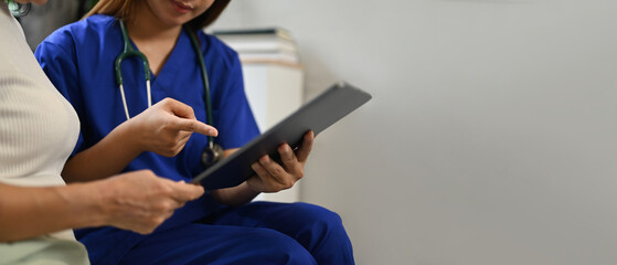 Female doctor showing digital tablet with results of some medical tests to senior woman patient