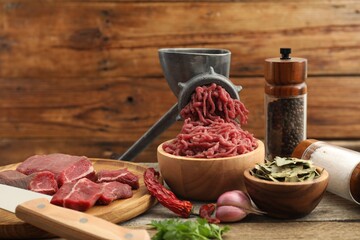 Manual meat grinder with beef, parsley and spices on wooden table